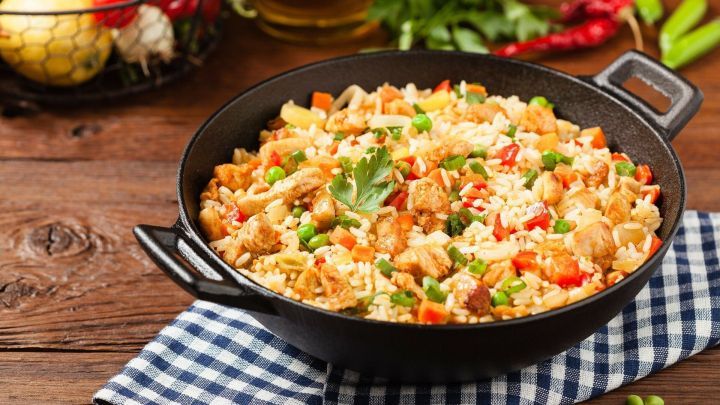 Eine schwere Pfanne mit bunter Chinapfanne, die auf einem karierten Tuch steht, umgeben von frischen Zutaten.