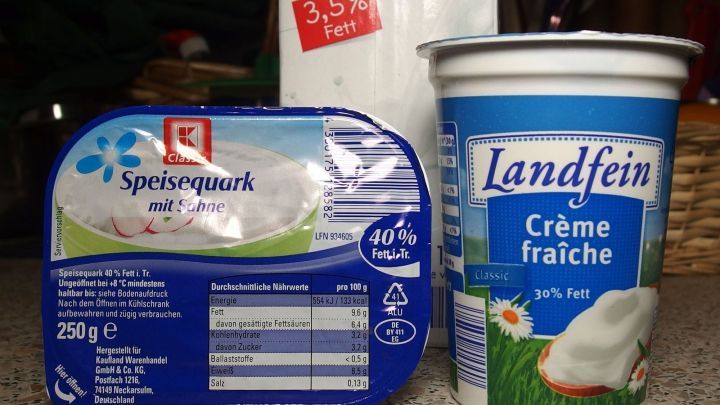 Ein Becher Cr&egrave;me fra&icirc;che und ein Paket Speisewaln stehen nebeneinander auf einer K&uuml;chenarbeitsplatte, um frische Zutaten zu zeigen.