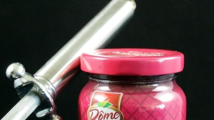 Ein Marmeladenglas mit einem drehbaren Verschluss steht neben einem &Ouml;ffnungswerkzeug auf dunklem Hintergrund.
