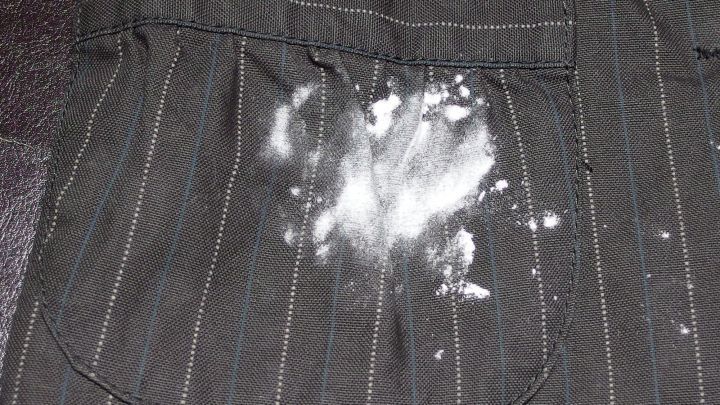 Ein Kleidungsst&uuml;ck mit einem gro&szlig;en Mehlflecken auf der Tasche liegt auf einem dunklen Untergrund.