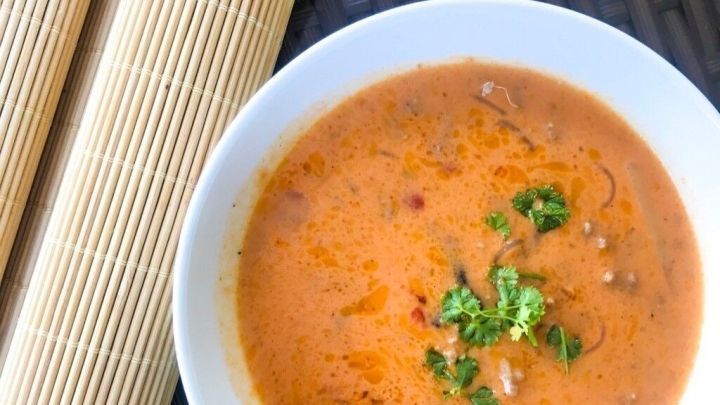 Eine Sch&uuml;ssel Lasagne-Suppe mit gr&uuml;ner Garnitur steht auf einem dunklen, strukturierten Untergrund, daneben liegen lasagne&auml;hnliche Platten.
