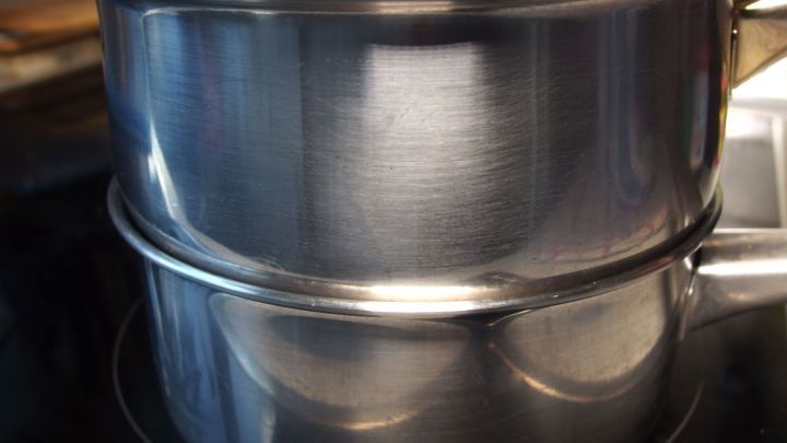 Ein gro&szlig;er Topf steht auf dem Herd und kocht Wasser, w&auml;hrend ein kleinerer Topf dar&uuml;ber dampft, um Strom zu sparen.