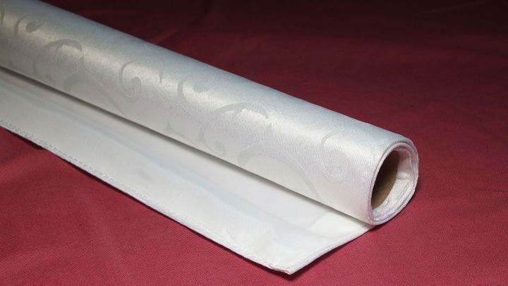 Eine gerollte Tischdecke liegt auf einem roten Untergrund, bereit zum Lagern und sp&auml;teren Gebrauch.