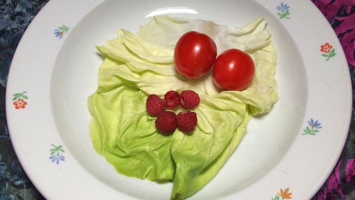 Ein Teller mit knackigem Salat und Himbeeren, garniert mit zwei roten Tomaten, im Mittelpunkt einer farbigen Umgebung.