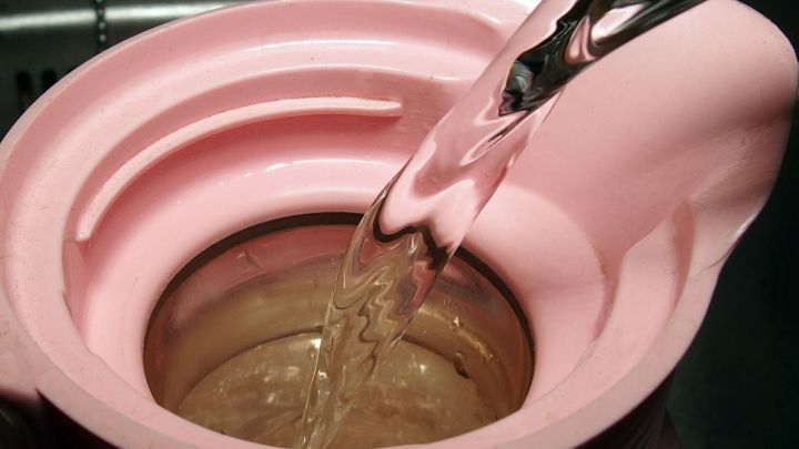 Eine pinke Thermoskanne wird mit hei&szlig;em Wasser gef&uuml;llt, um Kaffee darin l&auml;nger warmzuhalten.