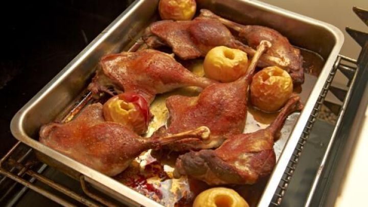 Saftige G&auml;nsekeulen liegen auf einem Blech im Ofen, umgeben von goldbraunem Obst, das zum Braten bereit ist.