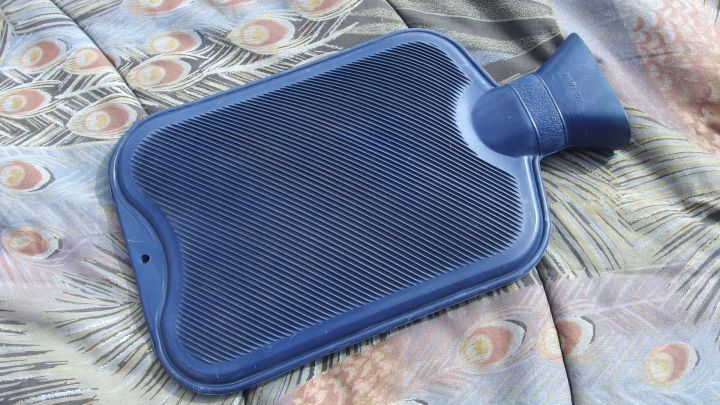 Eine W&auml;rmflasche liegt auf einem bunten Tuch und vermittelt W&auml;rme, um trotz leichter Unterleibsbeschwerden mobil zu bleiben.
