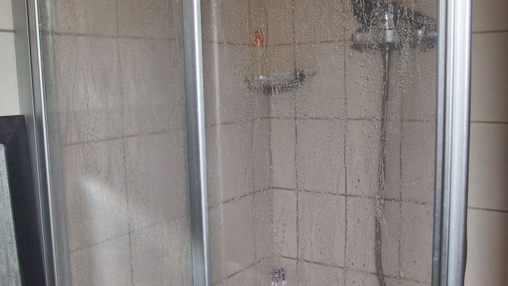 Eine Duschkabine mit kalkbeladenen Fliesen wird in einem Badezimmer gezeigt, wo der Wasserstrahl auf die Fliesen trifft.