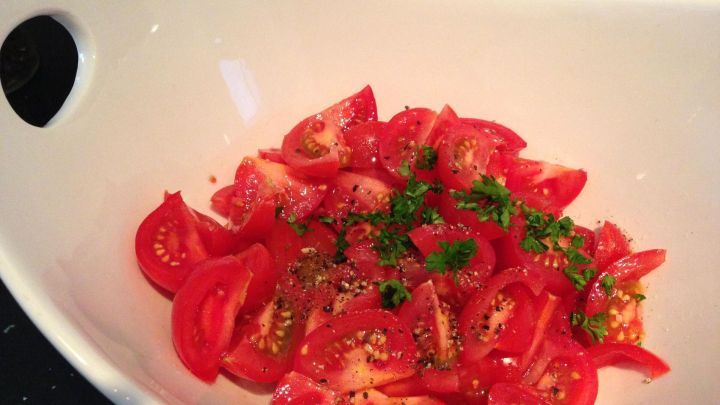 Tomatenst&uuml;cke mit gehacktem Gr&uuml;nzeug liegen in einer wei&szlig;en Sch&uuml;ssel, im Hintergrund liegt ein Messer auf dem Tisch.