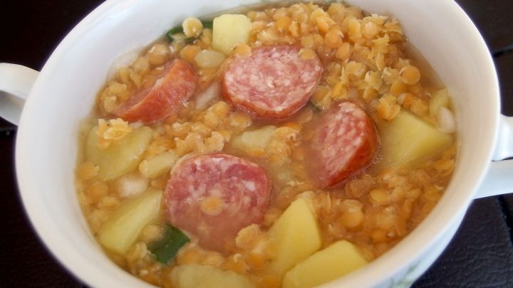 Eine cremige Linsensuppe mit St&uuml;ckchen von Wurst und Kartoffeln wird in einer wei&szlig;en Schale serviert.