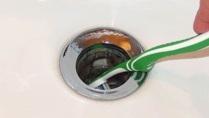 Eine Zahnb&uuml;rste mit gr&uuml;n-wei&szlig;en Borsten wird in einen Abfluss gesteckt, in einem hellen Waschbecken sichtbar.