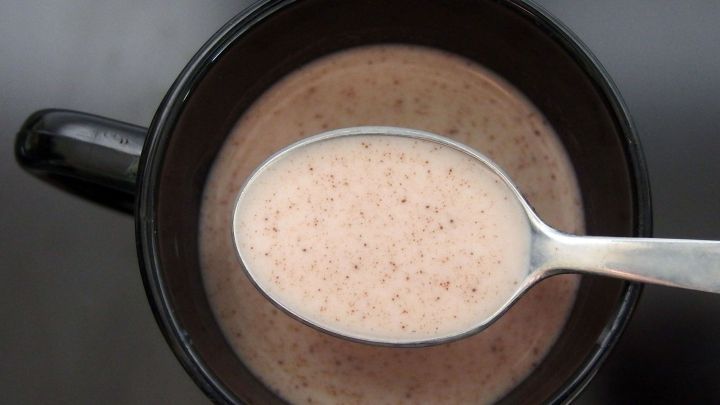 Ein schwarzer Becher mit kaltem Kakao, in dem ein L&ouml;ffel steckt, steht auf einer dunklen Oberfl&auml;che.