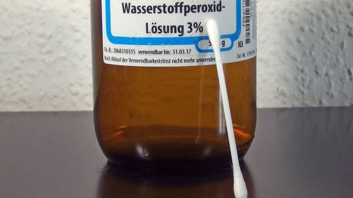 Eine Flasche mit Wasserstoffperoxid steht auf dem Tisch, während ein Wattestäbchen bereit ist, für die Anwendung.