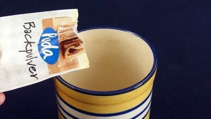 Eine Packung Backpulver wird &uuml;ber einen gelben Becher mit Streifen gehalten, um m&ouml;glicherweise Teer&auml;nder zu entfernen.