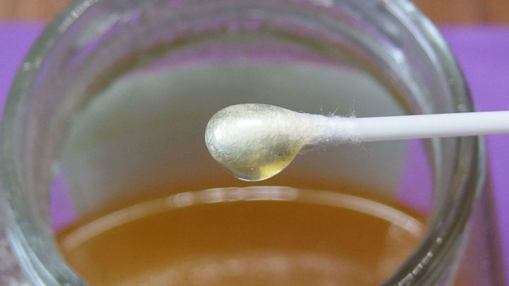Ein Wattest&auml;bchen mit Honig steht &uuml;ber einem Glas Honig, um ihn bei Schnupfen anzuwenden. Der Hintergrund ist unscharf.