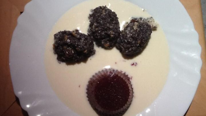 Mohnpielen serviert auf einem Teller mit Vanillesauce und Gelee im Muffinpapier, auf einem Holztisch pr&auml;sentiert.