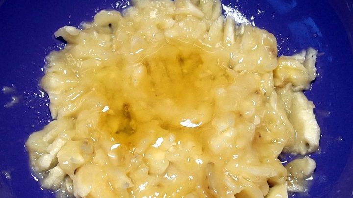 Eine zerdr&uuml;ckte Banane vermischt mit Honig liegt in einer blauen Sch&uuml;ssel, bereit zur Herstellung einer Feuchtigkeitsmaske.