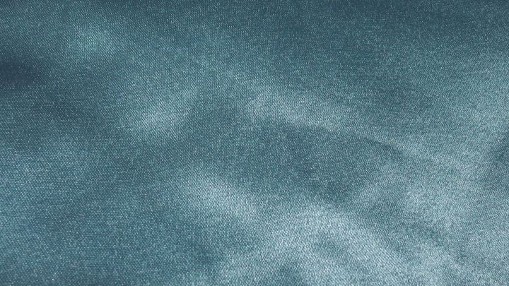 Ein schimmerndes Seidentuch liegt flach und zeigt feine, glatte Texturen in einem sanften, bl&auml;ulichen Farbton.