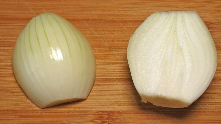 Eine geschnittene Zwiebel liegt auf einem Holzbrett, bereit zum Kochen, w&auml;hrend sie durch den Schnitt frische Aromen entfaltet.