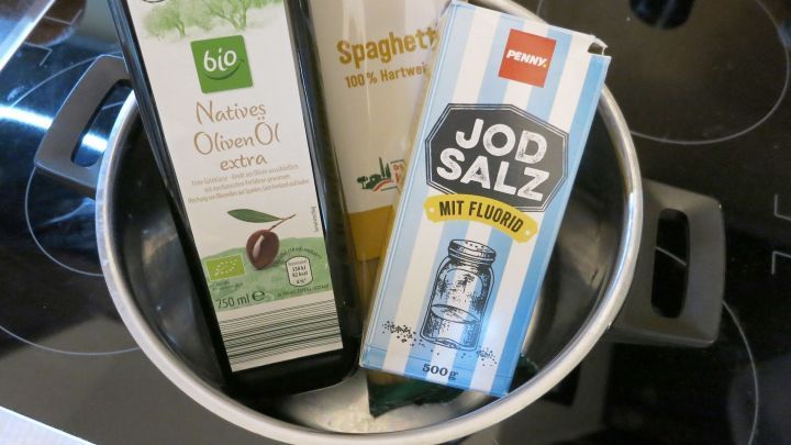 Ein Topf steht auf dem Herd, gef&uuml;llt mit Spaghetti und erg&auml;nzt durch Oliven&ouml;l und Jodsalz f&uuml;r das Pasta kochen.