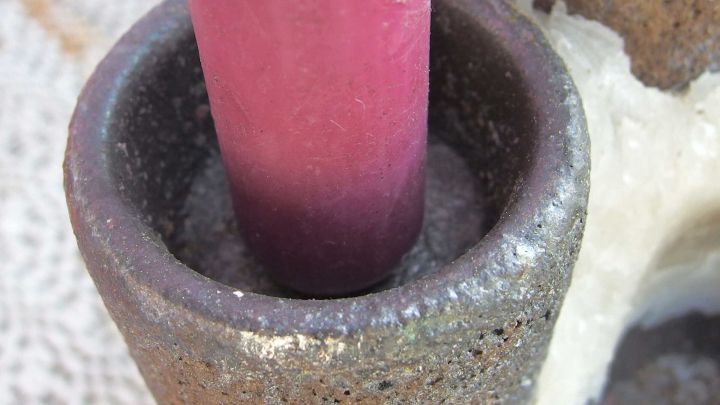 Eine kleine Kerze steckt in einem zu gro&szlig;en Kerzenst&auml;nder, der aus grauem Material gefertigt ist und auf einem Tisch steht.