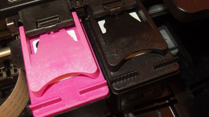 Eine pinke und eine schwarze Druckerpatrone liegen in einem Drucker, bereit zum Einsatz. Tinte könnte auf Fingern landen.