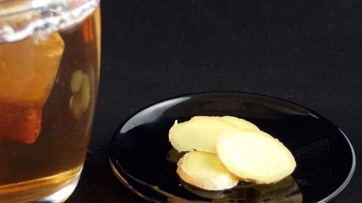 Eine Tasse Ingwertee steht neben einer kleinen Platte mit frischen Ingwerscheiben, alles vor einem dunklen Hintergrund.