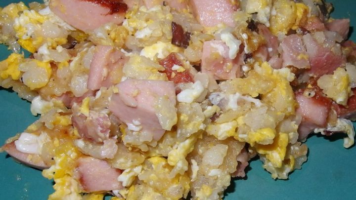 Ein Gericht aus Brat-Reis mit geschlagenen Eiern, Schinkenst&uuml;cken und Zwiebeln auf einem blauen Teller.