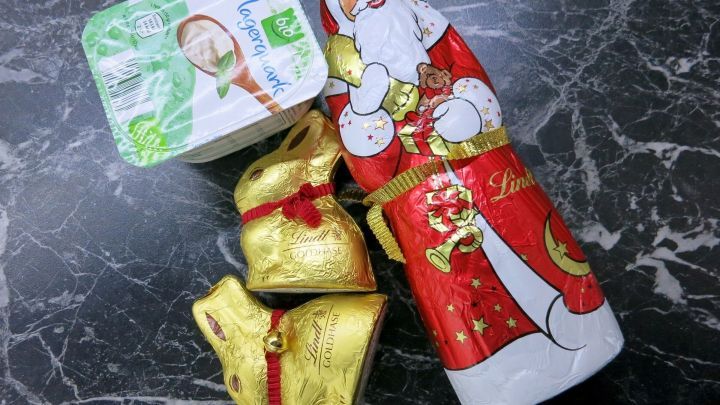 Ein weihnachtlich dekorierter Schokoladenmann steht neben kleinen goldenen Schokoladens&auml;ckchen und einer Schokoladentafel.