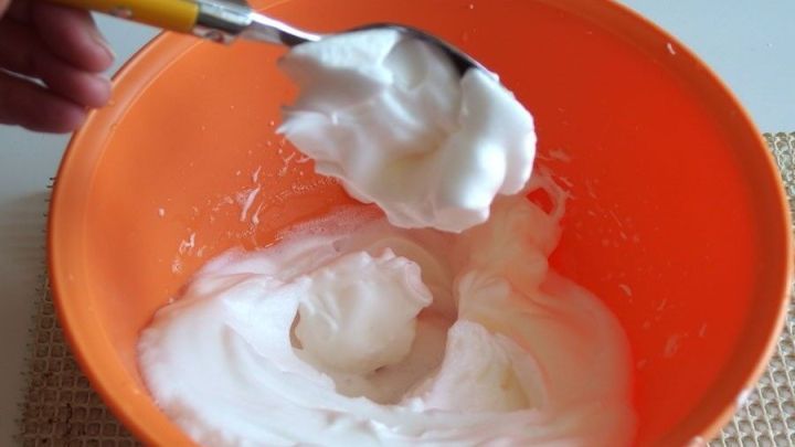 Eine Person hebt mit einem L&ouml;ffel steifen Eischnee aus einer orangefarbenen Sch&uuml;ssel, um ihn weiterzuverarbeiten.