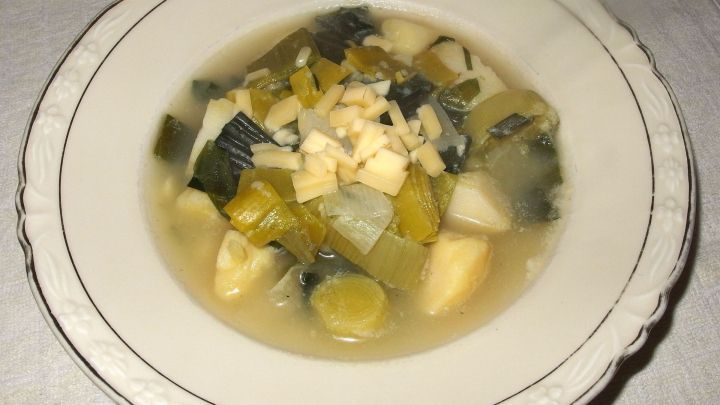 Ein Teller mit Saucenkartoffeln liegt auf einem Tisch. Die Kartoffeln sind in einer klaren Br&uuml;he mit Gem&uuml;sest&uuml;cken.