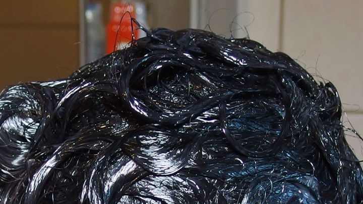 Kratzen von gef&auml;rbtem, gl&auml;nzendem Haar, w&auml;hrend es in einem Friseursalon vorbereitet wird. Die Umgebung ist neutral.