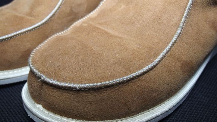 Helle Wildlederschuhe liegen nebeneinander, leicht verschmutzt und mit einem dunklen Hintergrund, bereit zur Reinigung.