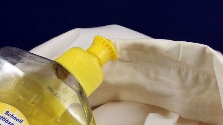 Eine Flasche mit gelbem Deckel steht nahe einem weißen Hemd, während Reinigungsmittel für das Entfernen von Kragenspeck verwendet wird.