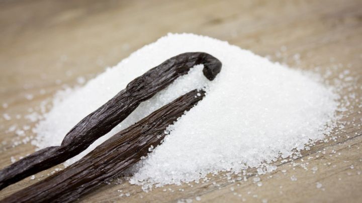 Eine Ansammlung von wei&szlig;em Zucker liegt neben einer vanilleschote auf einer Holzoberfl&auml;che und k&ouml;nnte Ger&uuml;che in der Wohnung beseitigen.