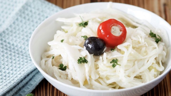 Ein frischer Wei&szlig;krautsalat liegt in einer wei&szlig;en Sch&uuml;ssel, garniert mit einer roten Kirsche, einer schwarzen Olive und Petersilie.