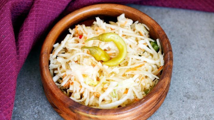 Ein Holzsch&auml;lchen mit frischem, gehobeltem Krautsalat und einer gr&uuml;nen Chili, auf einer grauen Oberfl&auml;che serviert.