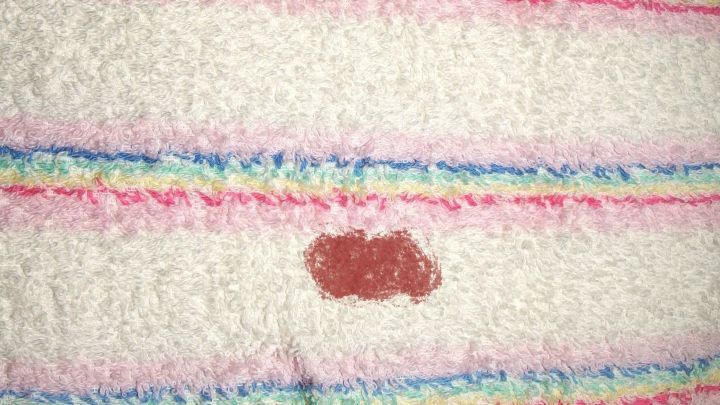 Auf einem hellen Handtuch mit bunten Streifen liegt ein roter Blutfleck, der eine sorgf&auml;ltige Entfernung erfordert.