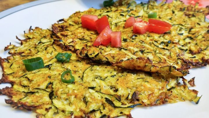Zucchinipuffer liegen auf einem Teller, garniert mit Tomatenst&uuml;cken und Fr&uuml;hlingszwiebeln, serviert in einer gem&uuml;tlichen K&uuml;che.