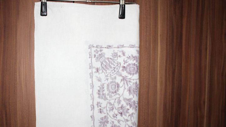 Ein wei&szlig;es Tischtuch h&auml;ngt an einer W&auml;scheleine, sorgf&auml;ltig gefaltet, um Knickfalten nach dem B&uuml;geln zu vermeiden.