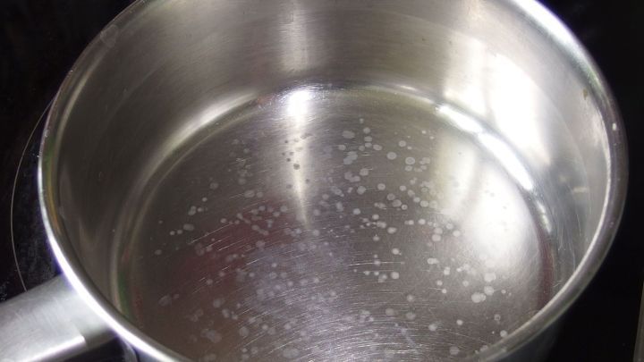 Ein kochender Topf mit Wasser zeigt Kalkflecken am Boden nach dem Eierkochen, auf einem Herd in einer K&uuml;che.