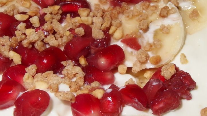 Eine cremige Joghurt-Sahne-Creme ist mit frischen Fr&uuml;chten, wie Granatapfelkernen und Bananenscheiben, garniert.