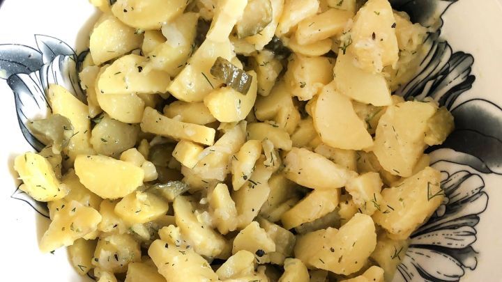 Ein Teller schw&auml;bischer Kartoffelsalat liegt vor einem bl&uuml;henden Telleruntersetzer, gut angerichtet und appetitlich.