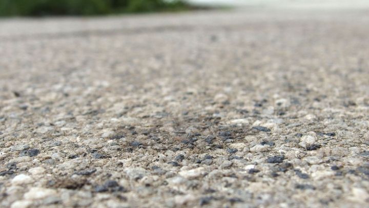 Auf dem Pflasterstein sind dunkle &Ouml;lflecken sichtbar, w&auml;hrend eine gr&uuml;ne Wiese im Hintergrund erkennbar ist.