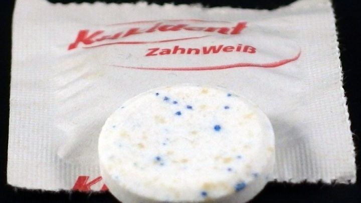 Ein Reinigungstablette liegt auf einer Verpackung. Die Tablette ist hell mit blauen und schwarzen Flecken, ideal gegen Ablagerungen.