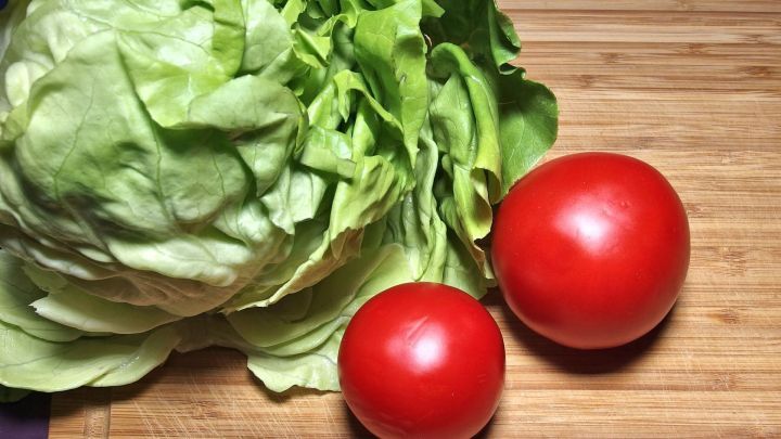 Frischer Salat, bestehend aus einem Kopfsalat und zwei roten Tomaten, liegt auf einem Holzbrett.