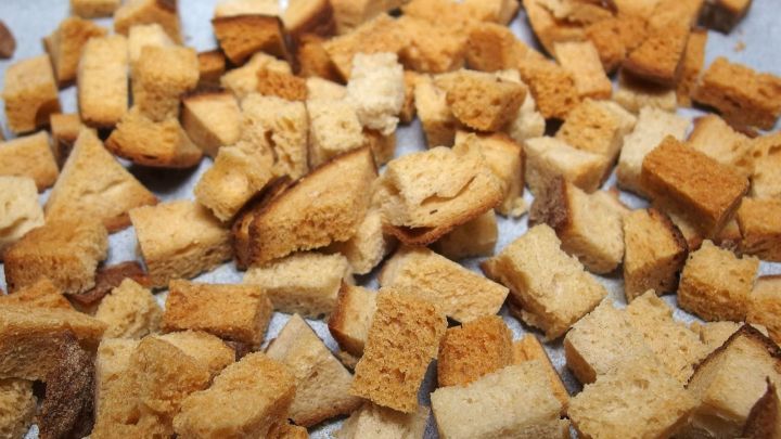 Kleine, goldbraune Croutons aus Brotresten liegen gleichm&auml;&szlig;ig auf einem Backblech in einer hellen K&uuml;che.