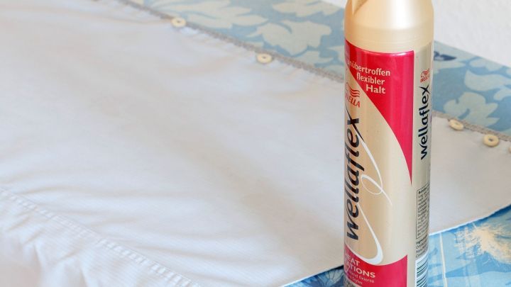 Eine Spraydose Haarspray steht neben einem blauen, bl&uuml;tenmusterbezogenen Stoff, bereit, um Teeflecken zu entfernen.