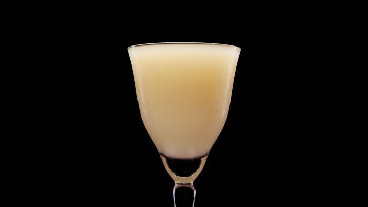 Ein elegantes Glas mit einem milchigen Getr&auml;nk steht vor einem schwarzen Hintergrund, das Licht reflektiert sanft darauf.