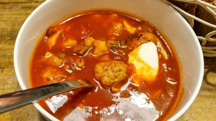 Eine Sch&uuml;ssel mit scharfer Hack-Gem&uuml;se-Suppe wird mit einem L&ouml;ffel serviert, umgeben von frischem Brot.